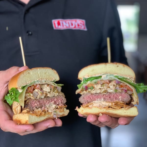 Hands holding two halves of a Lindy's burger, revealing a juicy patty and fresh toppings.