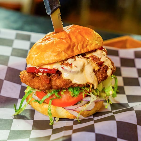 Lindy's on 4th burger with a thick patty, lettuce, tomato, onion, and sauce, on checkered paper.