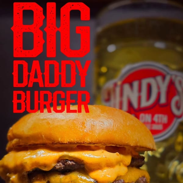 A Lindy's on 4th "Big Daddy Burger" with melted cheese and two patties, with a pickle jar in the background.