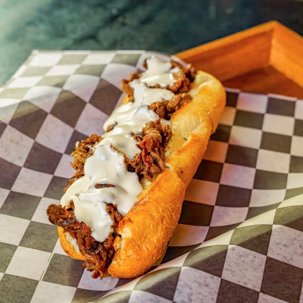 Cheesesteak sandwich with melted white cheese and meat on a checkered paper, from Lindy's on 4th.