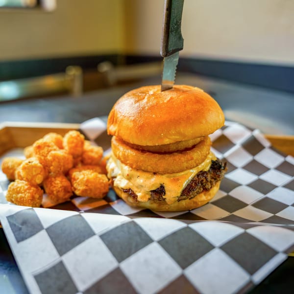 Lindy's on 4th burger with onion rings, special sauce, and tater tots on checkered paper.