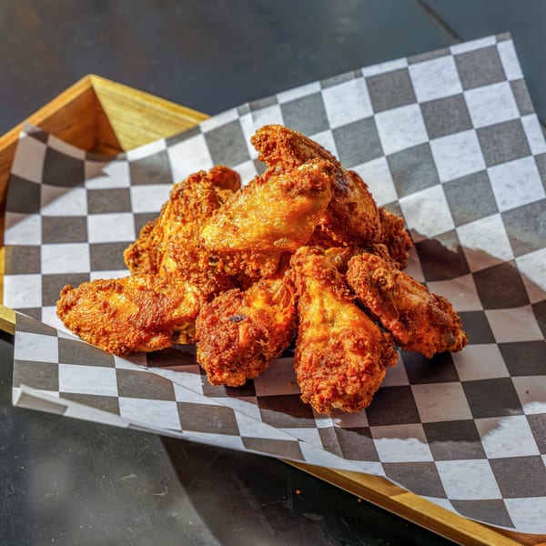 Crispy fried chicken wings piled on checkered paper in a wooden tray at Lindy's on 4th.