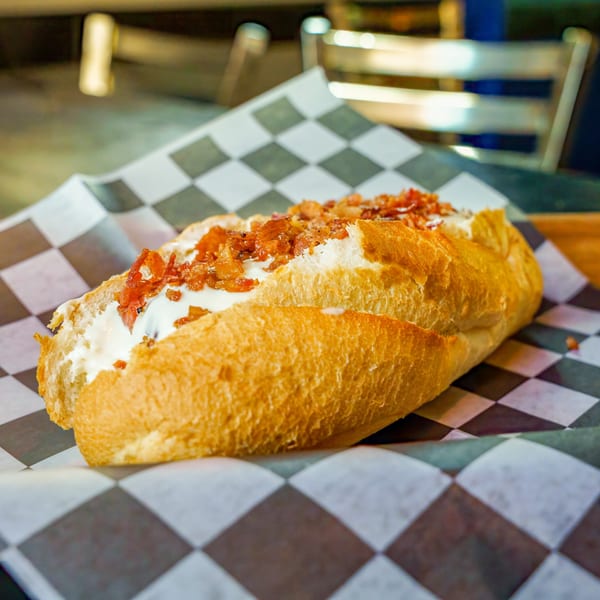 A Lindy's on 4th hot dog with cream cheese and bacon bits on checkered paper.