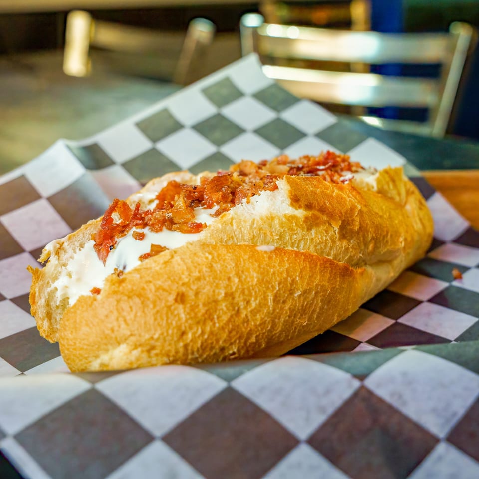 A Lindy's on 4th hot dog with cream cheese and bacon bits on checkered paper.