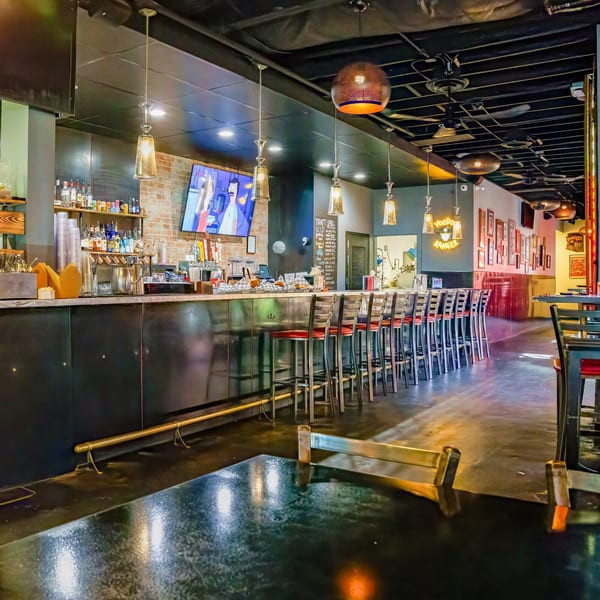 Interior of Lindy's on 4th, featuring a long bar with stools, a TV, and neon signs.