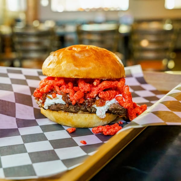 Lindy's on 4th burger with Cheetos, caramelized onions, and white sauce on checkered paper.
