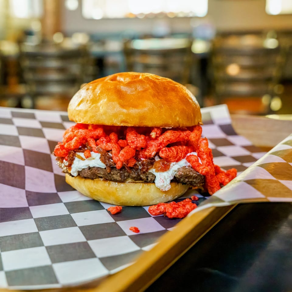 Lindy's on 4th burger with Cheetos, caramelized onions, and white sauce on checkered paper.