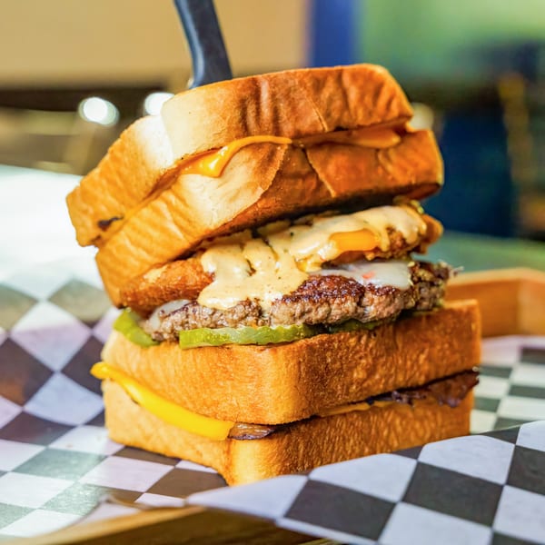 A towering Lindy's burger with multiple patties, cheese, pickles, and sauce, served on toasted bread.
