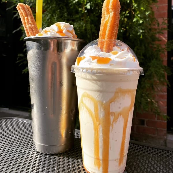 Two churro milkshakes with whipped cream and caramel drizzle, one in a metal cup, one in plastic.