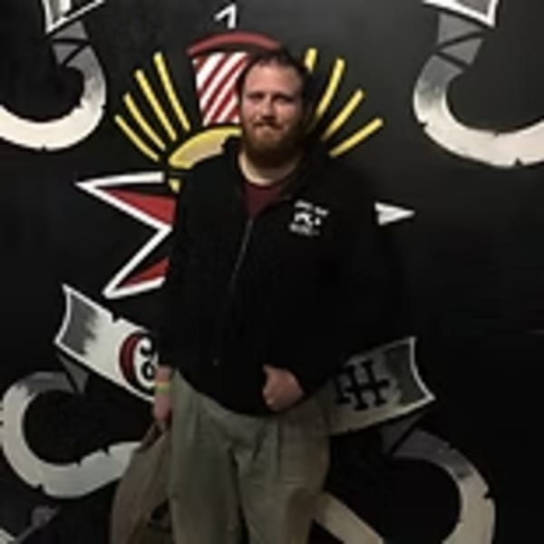 Man with a beard standing in front of a black wall with Lindy's on 4th burger-themed art.