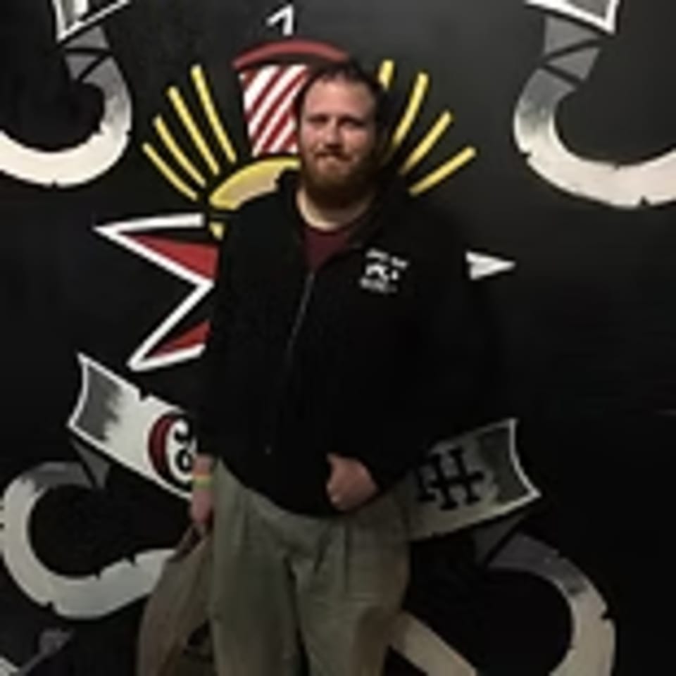 Man with a beard standing in front of a black wall with Lindy's on 4th burger-themed art.