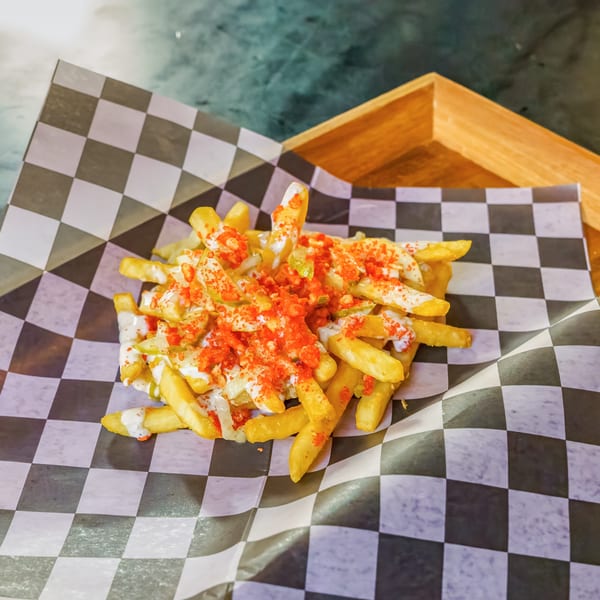 Lindy's on 4th fries, topped with white sauce and red seasoning, on checkered paper.