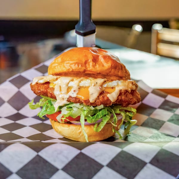 A Lindy's on 4th burger with a fried patty, melted cheese, and sauce, on checkered paper.