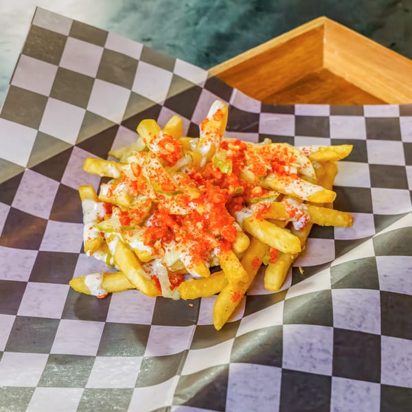 Lindy's on 4th fries, topped with white sauce, red seasoning, and green relish on checkered paper.