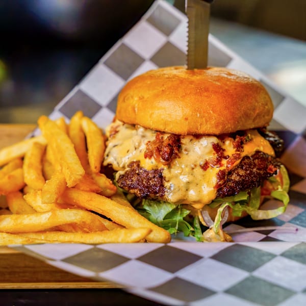 A Lindy's on 4th burger with melted cheese, bacon, lettuce, and fries on checkered paper.