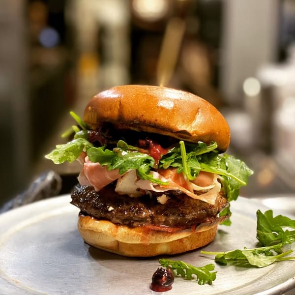 A gourmet burger from Lindy's on 4th, topped with prosciutto, arugula, and a sweet sauce.