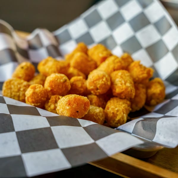 Golden-brown tater tots served in a black and white checkered paper-lined basket.