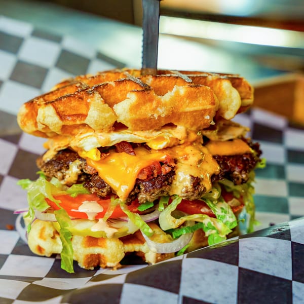 A Lindy's on 4th waffle burger with two patties, cheese, bacon, egg, and vegetables.
