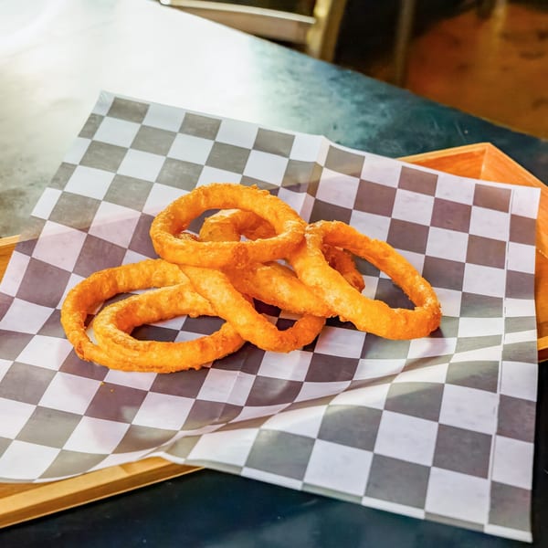 Golden-brown onion rings served on checkered paper in a wooden tray at Lindy's on 4th.