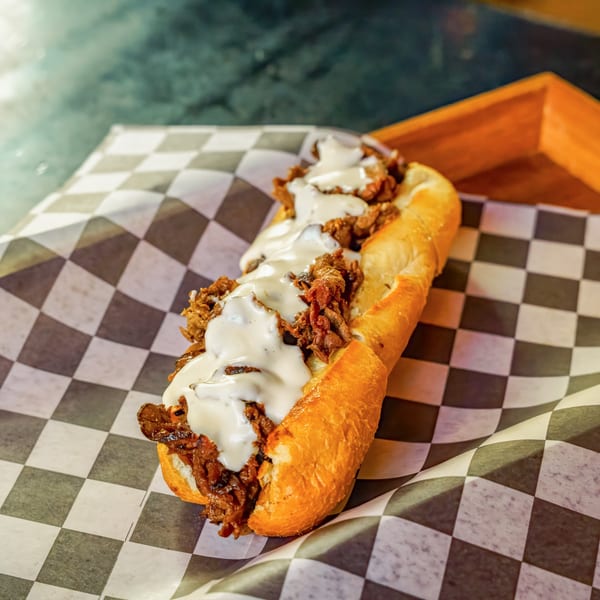 A Lindy's on 4th cheesesteak sandwich with melted white cheese on a checkered paper.