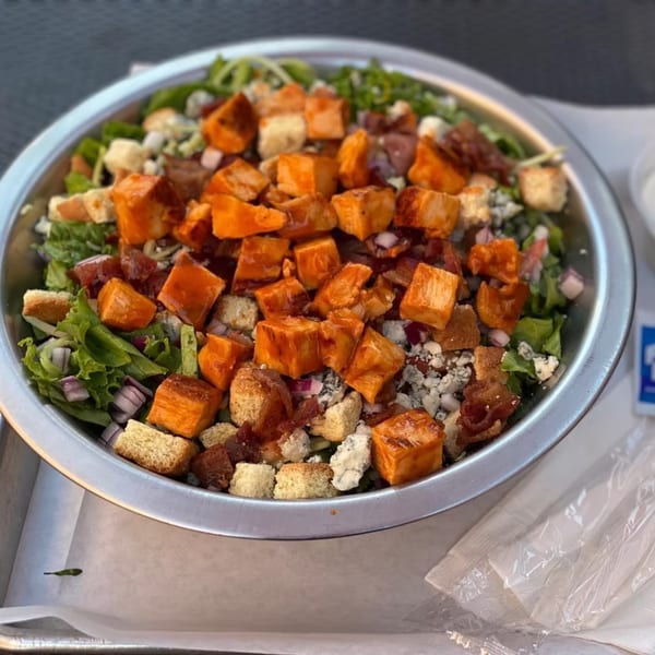 A metal bowl filled with a salad topped with buffalo chicken, bacon, blue cheese, and croutons.
