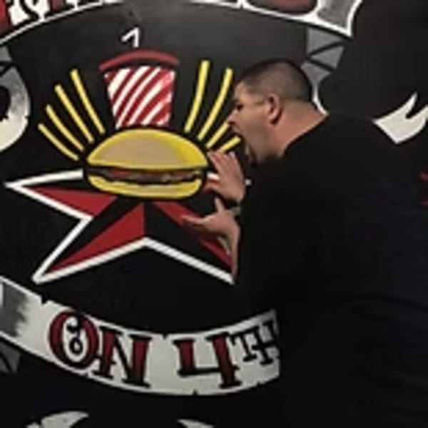 Man pretending to eat a burger from a large Lindy's on 4th mural with a star and soda.