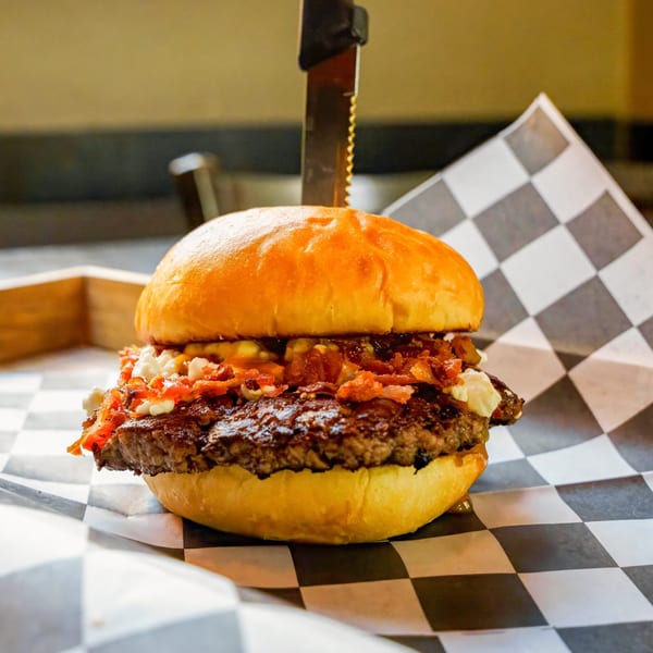 A Lindy's on 4th burger with bacon, cheese, and a knife on checkered paper.