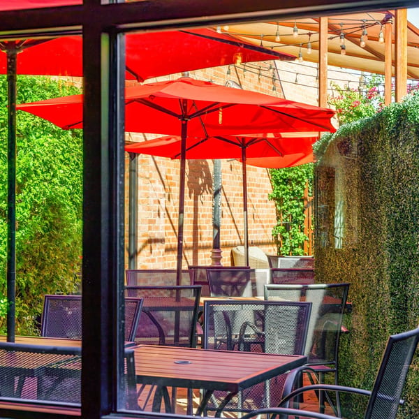 Outdoor patio at Lindy's on 4th with red umbrellas, metal tables, and lush green foliage.