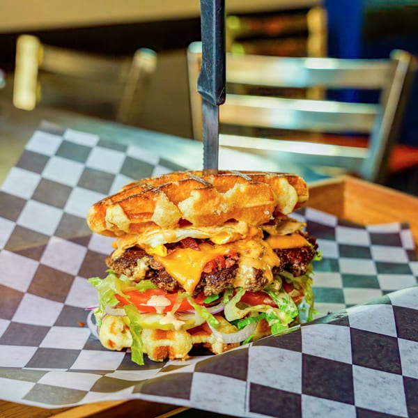 Lindy's on 4th waffle burger with two patties, cheese, bacon, egg, lettuce, tomato, and onion.