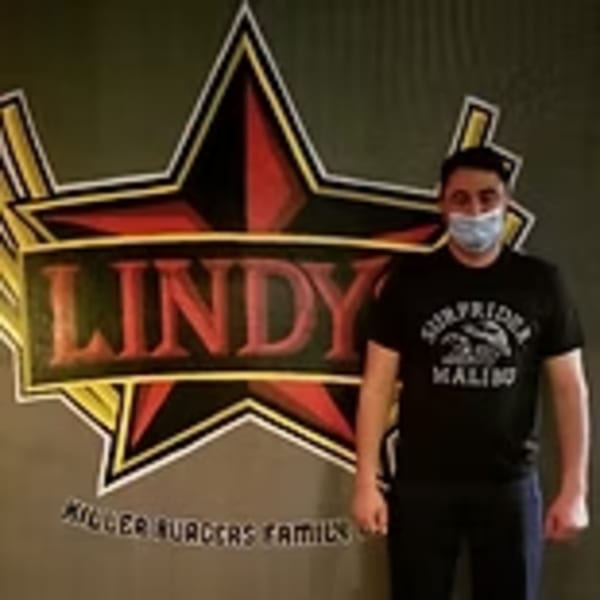 Man in a mask and black shirt standing in front of Lindy's on 4th logo.